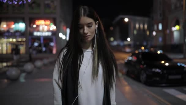 Mujer solitaria caminando por la noche en el centro de la ciudad escuchando música en auriculares — Vídeo de stock