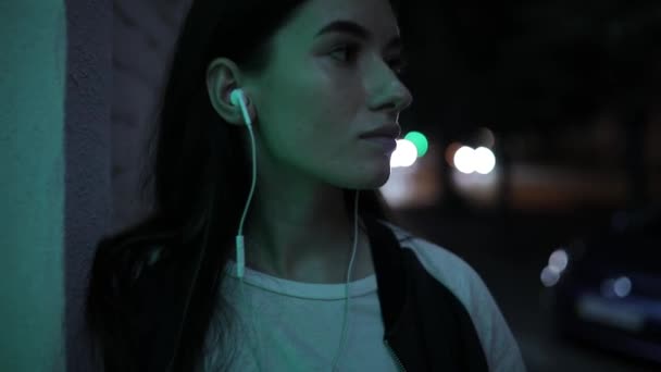 Mujer escuchando música y relajándose apoyada en la pared en la calle nocturna — Vídeo de stock