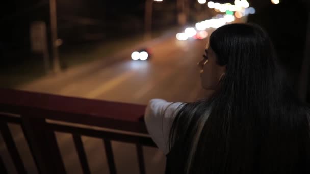 Mujer joven escuchando música de pie en un puente por la noche — Vídeos de Stock