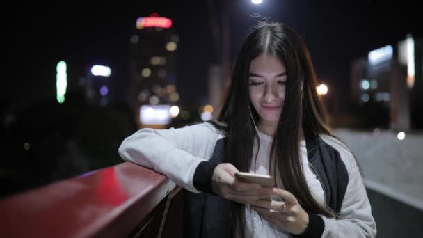 Jovem mulher usar aplicativos de smartphone em pé em uma ponte à noite — Vídeo de Stock