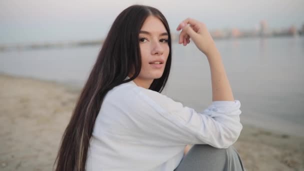 Nehir kumsalda oturma sevimli genç kadın portre — Stok video