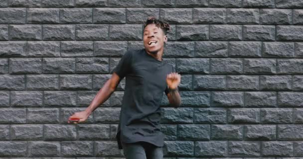 Hombre afroamericano bailando contra pared de ladrillo escuchando música — Vídeo de stock