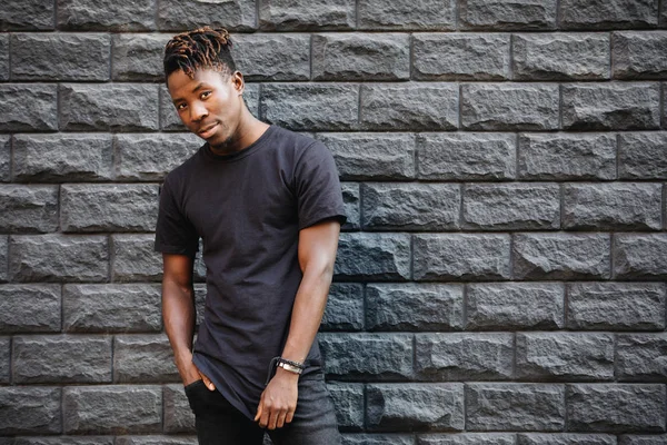 African american fashion male model in blank black t-shirt standing against brick wall