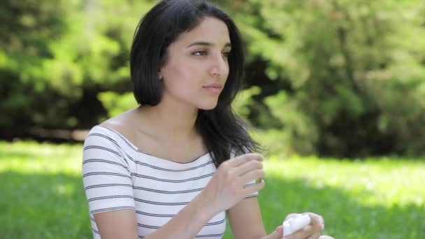 Молодая женщина вставила беспроводные воздушные стручки в уши, сидя на траве — стоковое видео