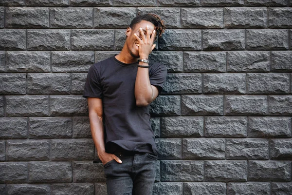 African american man in black t-shirt laughing against brick wall, palm on face