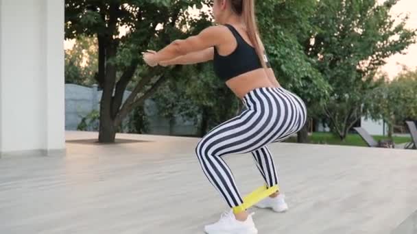 Donna adulta accovaccia all'aperto con fascia di resistenza, allenamento di fitness domestico — Video Stock
