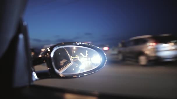 Водіння автомобіля в вечірньому місті, вид з салону в дзеркало заднього виду, розмитий дорожній фон — стокове відео