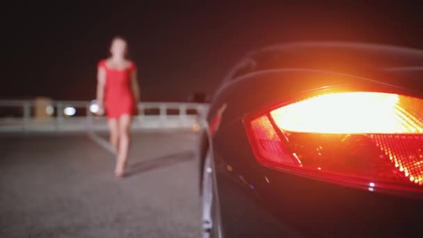Vrouw in sexy rode jurk gaan naar haar auto in nacht stad uitschakelen signalering — Stockvideo