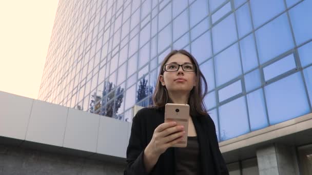 Geschäftsfrau mit Smartphone unter hohen Bürogebäuden, Ansicht von unten — Stockvideo