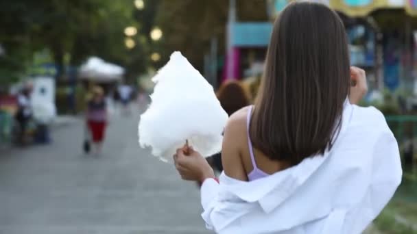 Chica feliz comiendo algodón de azúcar en un parque — Vídeos de Stock