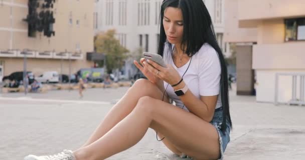 女性が市にイヤホンと携帯電話を使用して — ストック動画