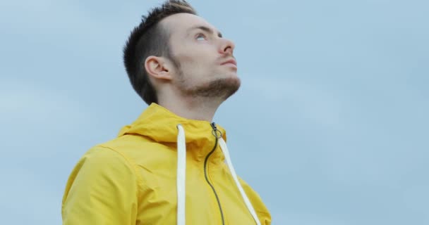 Man in yellow jacket looking around cloudy sky background, weather concept — Stock Video