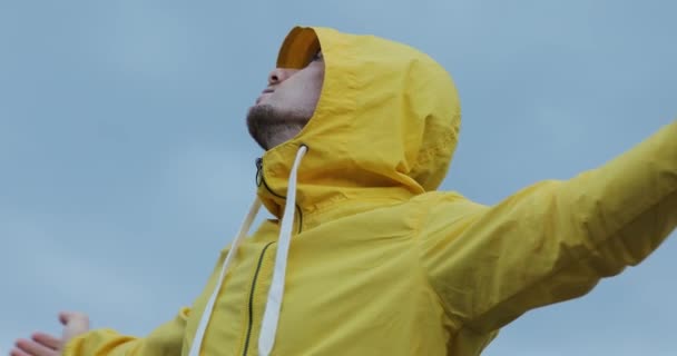 Hombre de chaqueta amarilla con las manos levantadas disfrutar nublado nublado cielo cielo fondo — Vídeo de stock