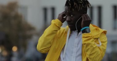 Şehir sokak kulaklık üzerine sarı ceket koyar mutlu Afrika adam zevk müzik