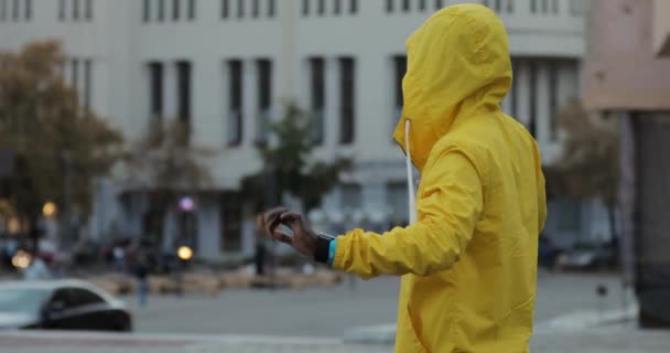 Homem africano de casaco amarelo dançando na rua da cidade ouvindo música — Vídeo de Stock