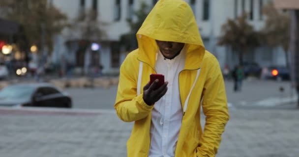 Αφρικανική άνθρωπος χρησιμοποιώντας smartphone με ακουστικά σε αστική πόλη το βράδυ — Αρχείο Βίντεο