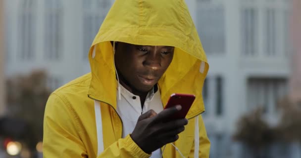 Hombre africano usando teléfono inteligente con auriculares en la ciudad urbana de la noche — Vídeos de Stock