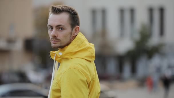 Portrait of young caucasian confident man wear hood of yellow windbreaker in city — Stock Video