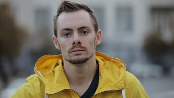 Ritratto di giovane uomo sicuro di sé caucasico indossare giacca a vento gialla e cappuccio in città — Video Stock