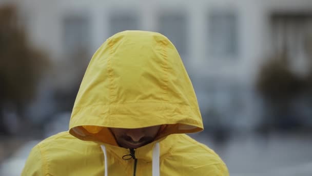 Портрет неузнаваемого человека в желтом капюшоне поднимает голову в городе — стоковое видео