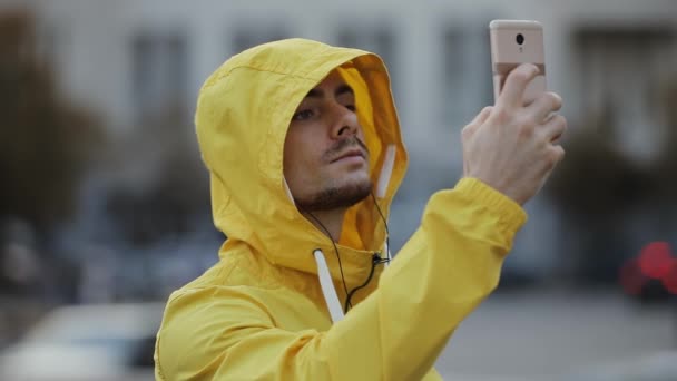 Retrato del turista en capucha amarilla tomando foto móvil en plaza urbana viajando — Vídeos de Stock