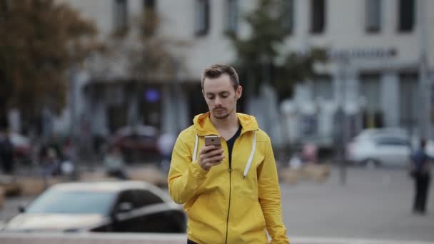 Homme en veste jaune en utilisant smartphone textos messages de navigation un téléphone mobile, communiquer marcher dans la ville — Video