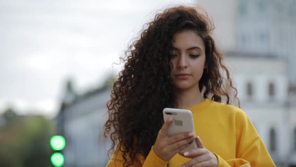 Menina adolescente no pullower amarelo usando mensagens de texto de smartphone um telefone celular, se comunicar na cidade — Vídeo de Stock