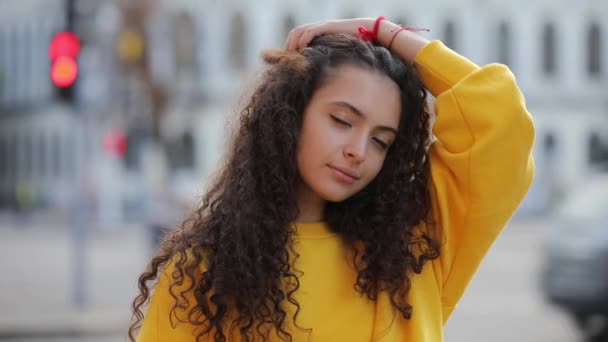 Mosolygó aranyos göndör tini lány portréja a sárga trikót, városi háttér — Stock videók