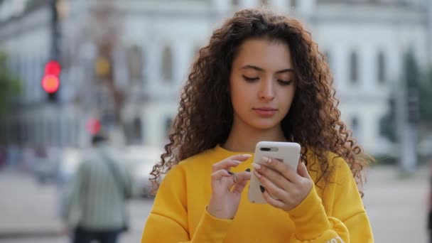 Chica adolescente en el pulidor amarillo usando mensajes de texto de teléfonos inteligentes un teléfono móvil, comunicarse en la ciudad — Vídeo de stock