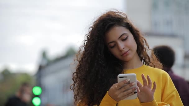 Tiener meisje in gele pullower met smartphone SMS berichten van een mobiele telefoon, communiceren in de stad — Stockvideo