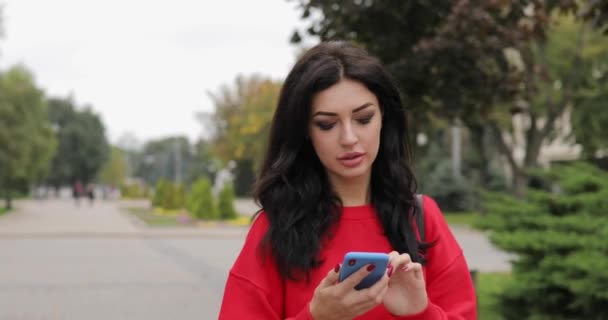 Женщина разговаривает со смартфоном, гуляя по городу — стоковое видео