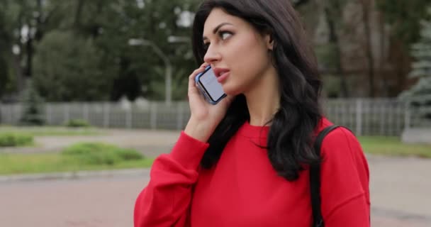 Woman in red blouse talking by smartphone going in city alley — Stock Video