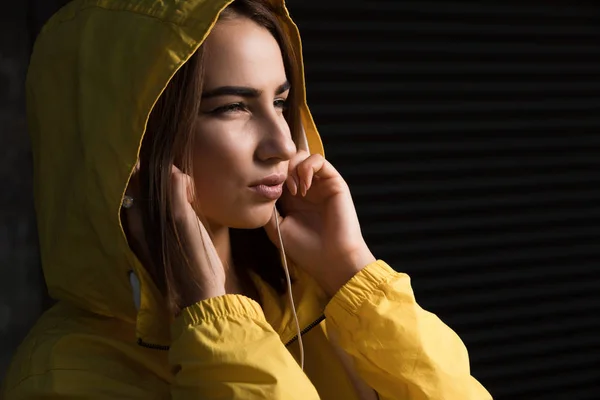 Mujer Seria Bajo Capucha Amarilla Con Auriculares Escuchando Una Música —  Fotos de Stock