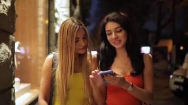 Genç kadın arkadaşlar aşağı bakıyor smartphone vasıl gece şehirde yürüyüş