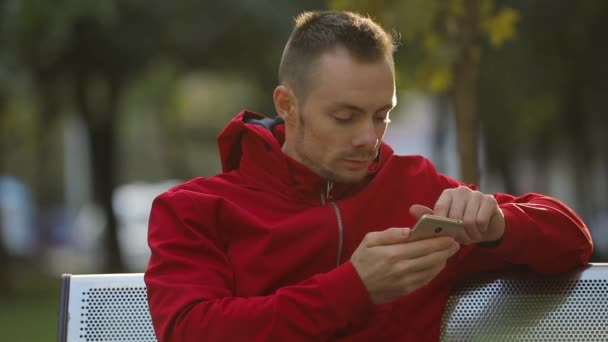 Joven Con Chaqueta Roja Llama Amigo Por Teléfono Inteligente Sentado — Vídeo de stock