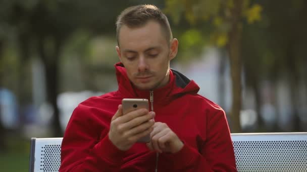 Mladý Muž Červené Bundě Pomocí Chytrého Telefonu Sedí Lavičce — Stock video