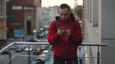 City, yolda arka plan Akıllı telefon kullanarak kırmızı ceketli genç adam