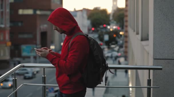 年轻人穿着红色夹克 在城市 道路上的背景下使用智能手机 — 图库视频影像