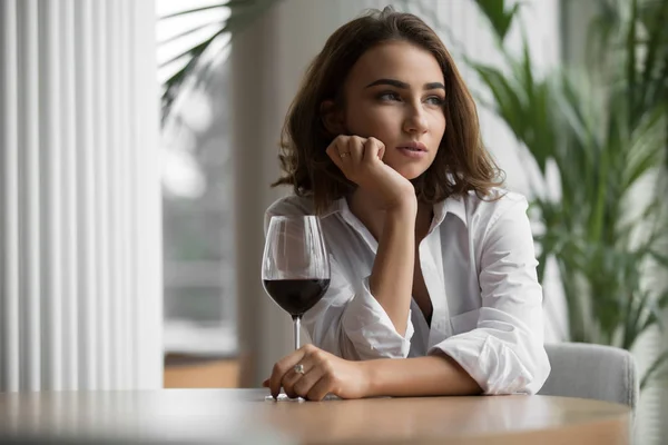 Woman alone with red wine glass sitting in the restaurant and thinking leaning head to hand