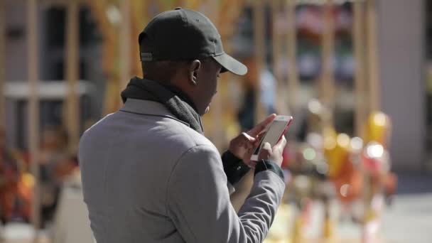 Черный мужчина использует смартфон в городе — стоковое видео