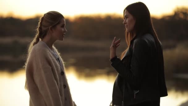 Discussie, twee vrouwen vrienden praten samen permanent aan rivier na zonsondergang, lachen en giechelen — Stockvideo