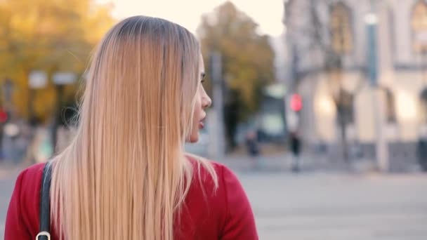 Привлекательная блондинка в красной ходьбе в осеннем городе, вид сзади, замедленная съемка — стоковое видео