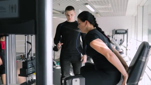 Entrenador de fitness personal corrige a la mujer deportiva principiante en el gimnasio — Vídeo de stock