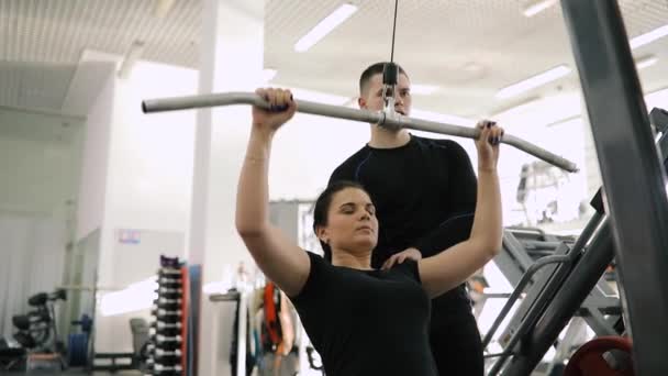 Entrenador de fitness personal que ayuda a hacer ejercicio para la mujer principiante en el gimnasio — Vídeo de stock