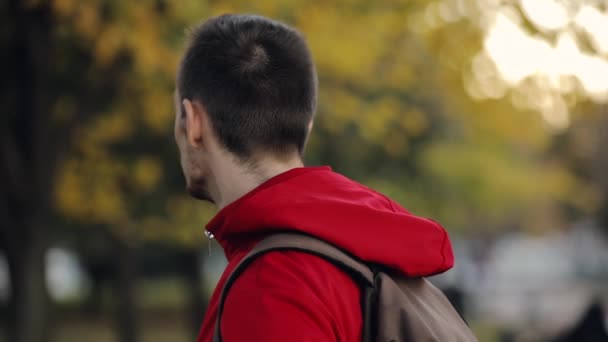 Mannen i röd jacka svarvning ansikte och tittar på kameran, höstdag — Stockvideo