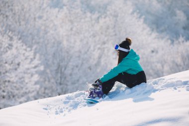 Yüksek tepe ve geri kalanı üzerinde oturan kadın snowboard