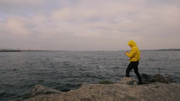 Caminata hombre viajero en chaqueta amarilla caminando solo en el río, tomar una foto por teléfono inteligente — Vídeo de stock