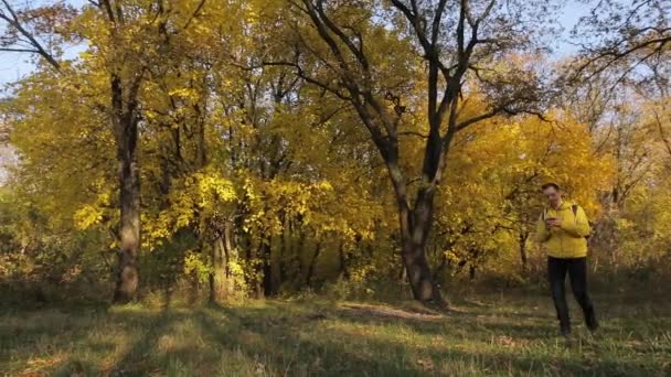 Uomo in giacca gialla che cammina con smartphone nella foresta autunnale — Video Stock