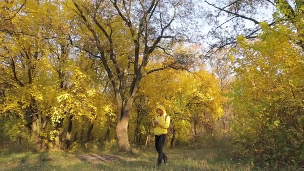 Человек в жёлтой одежде гуляет со смартфоном в осеннем лесу — стоковое видео