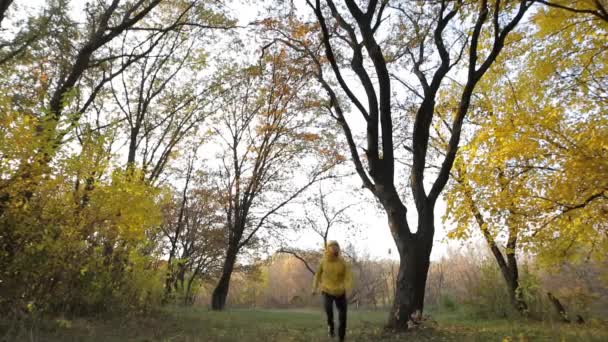 Счастливчик в желтой куртке бегает по осеннему лесу — стоковое видео